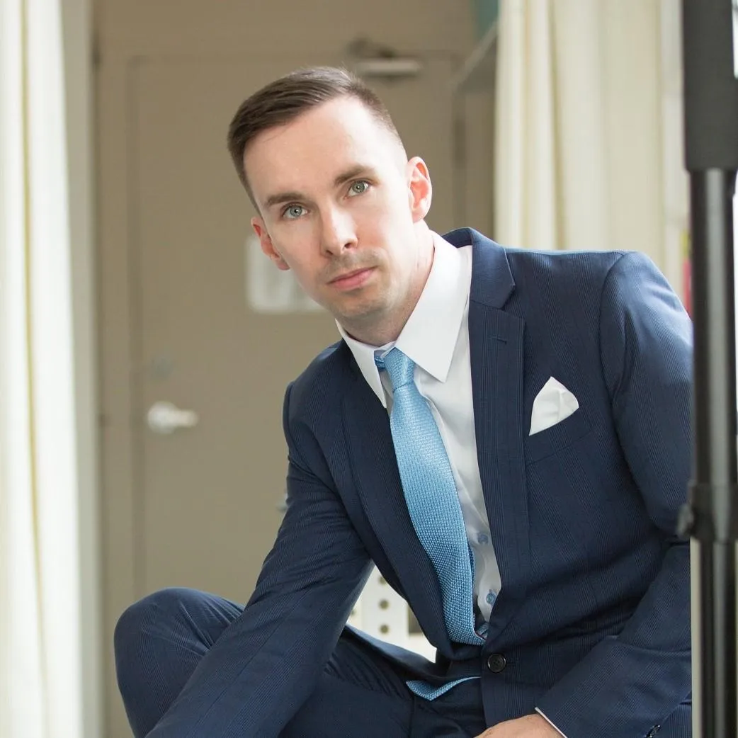 A man in a the essential navy suit, white dress shirt, light blue tie and white pocket square
