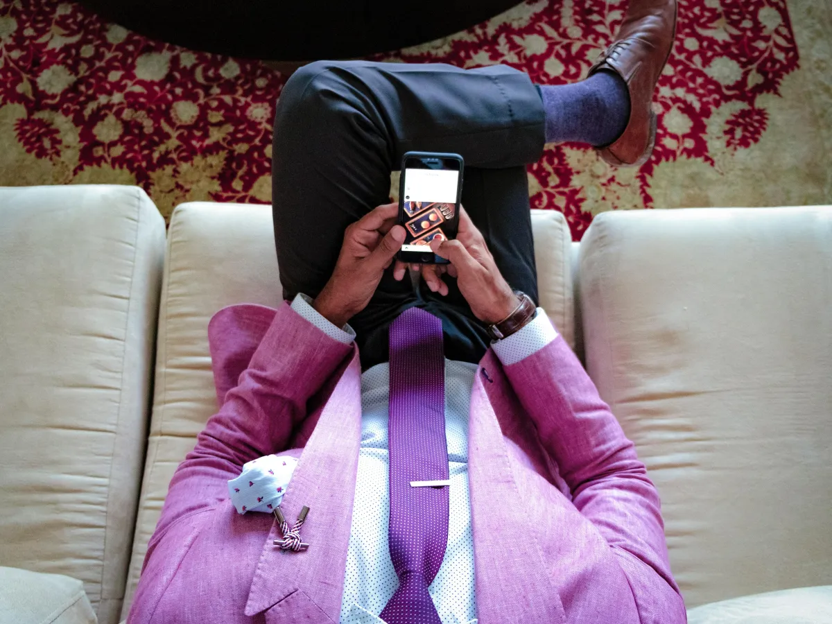 A man wearing a bold pink blazer, dark purply pink tie, white dress shirt, white pocket square and charcoal dress pants