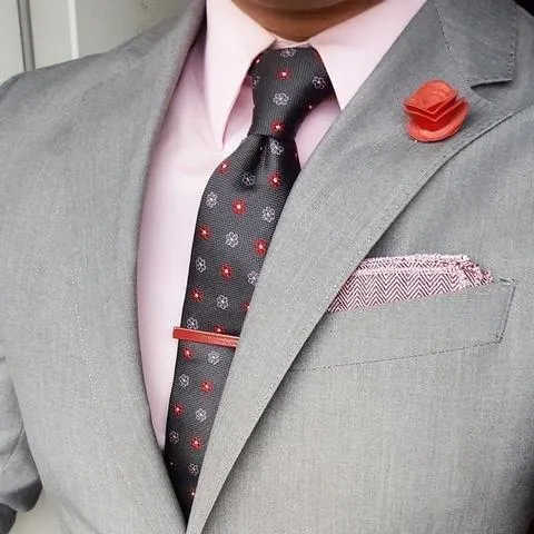 A man in a light grey suit with a light pink shirt, a tie, pocket square and lapel pin