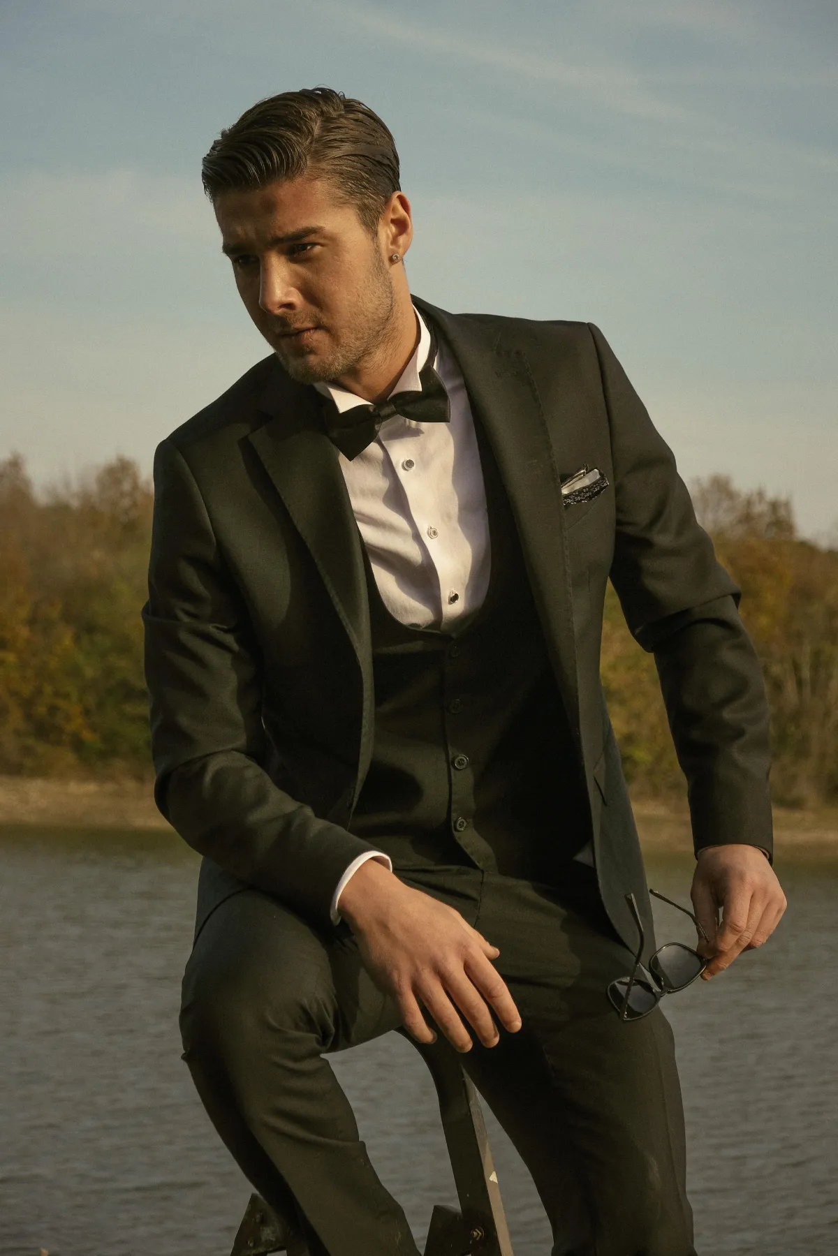 A man in a black suit with a black vest, white dress shirt, black bow tie and white pocket square