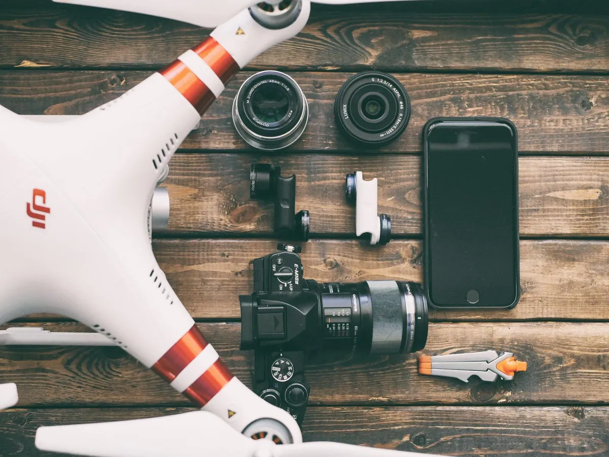 A camera, an iPhone and a drone laying on a wooden table.