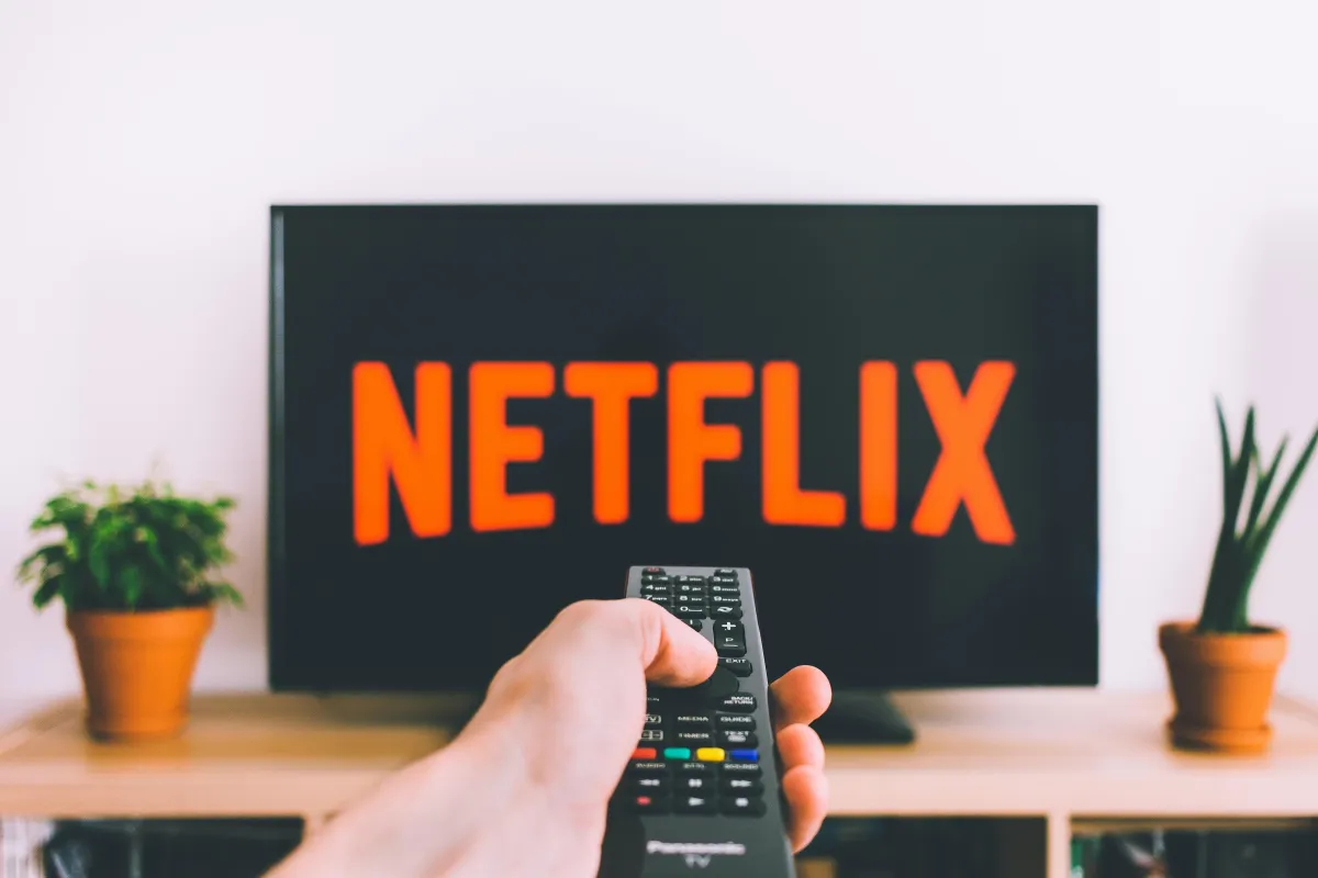 A hand holding a TV remote pointed at a TV with the Netflix logo on it.