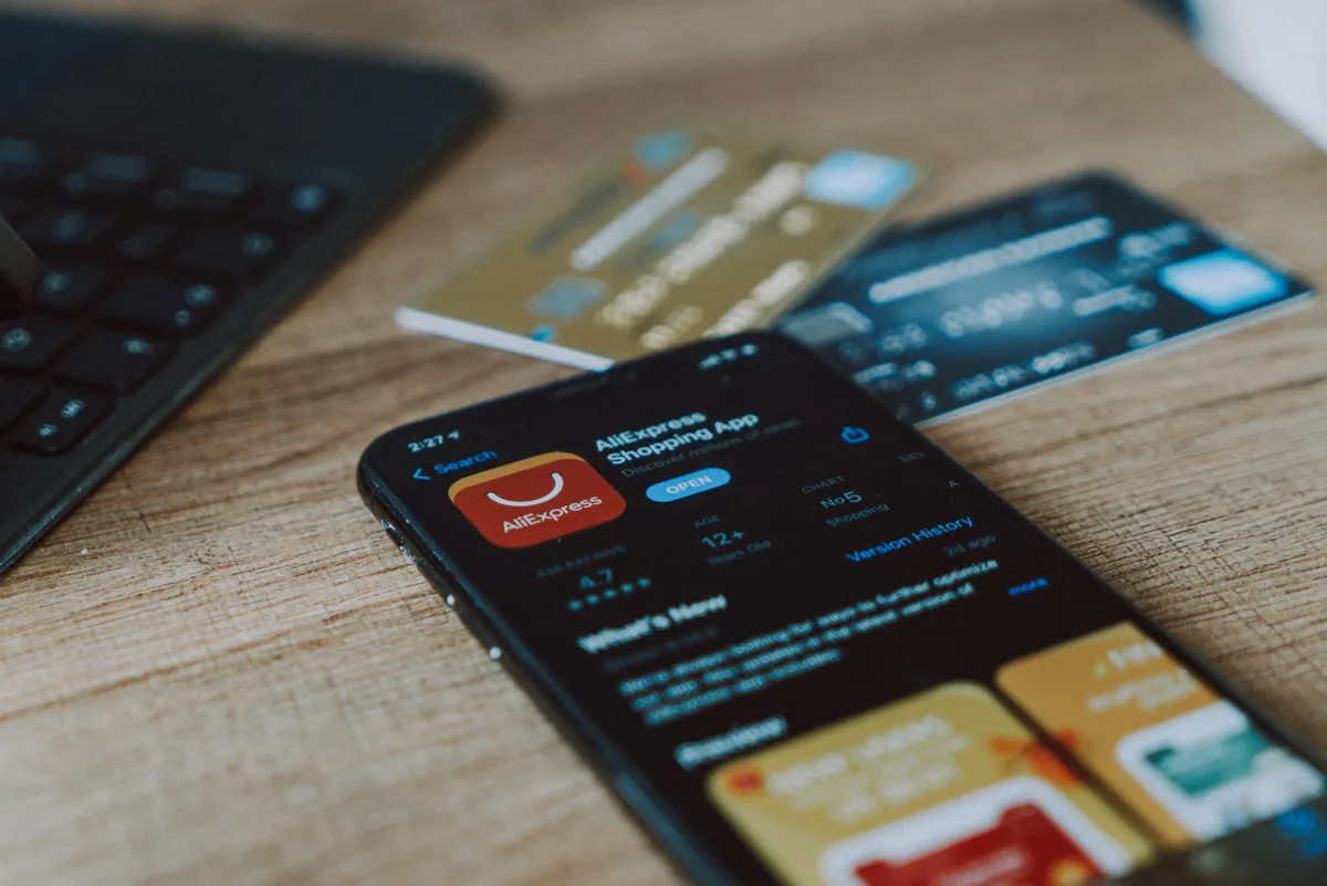 An iPhone showing the app AliExpress next to two bank cards.