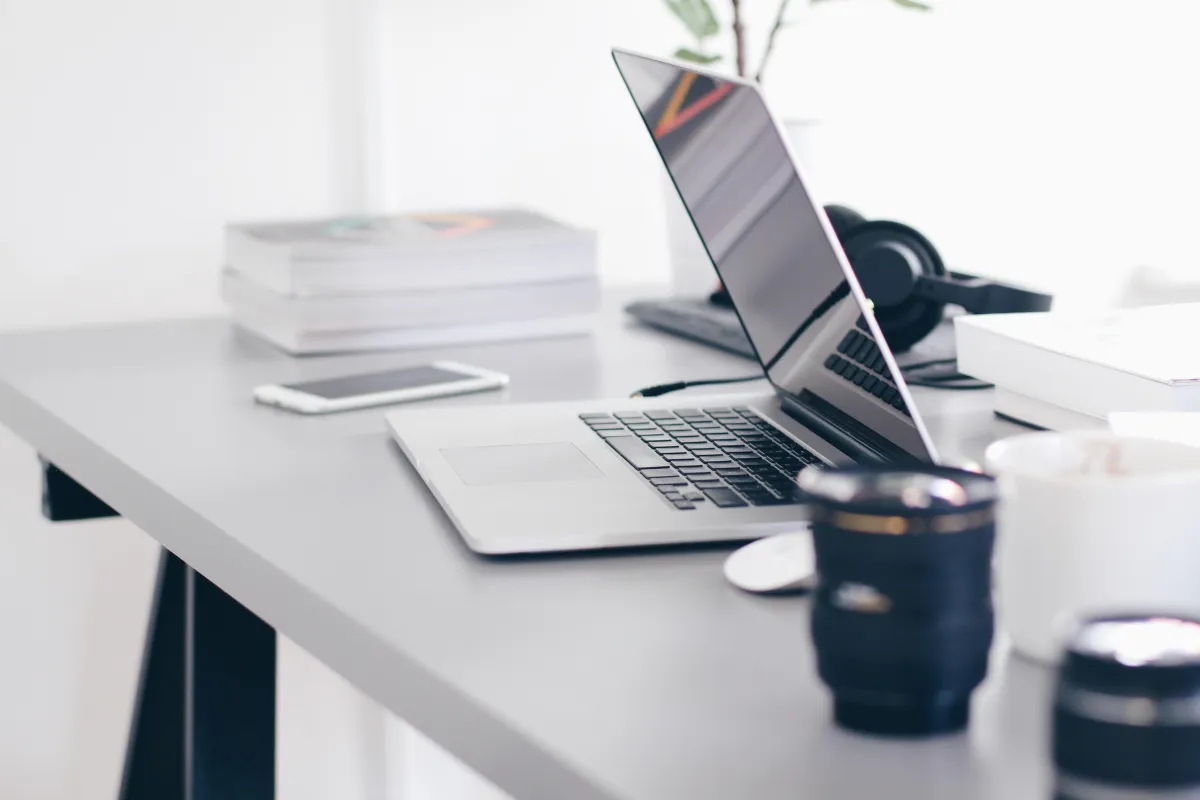 A laptop half open on a desk surrounded by mugs and papers.