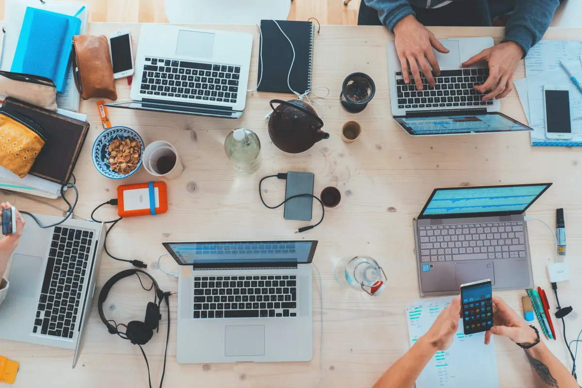 People sitting at a table with an assortment of different laptops, pencil cases and notes,