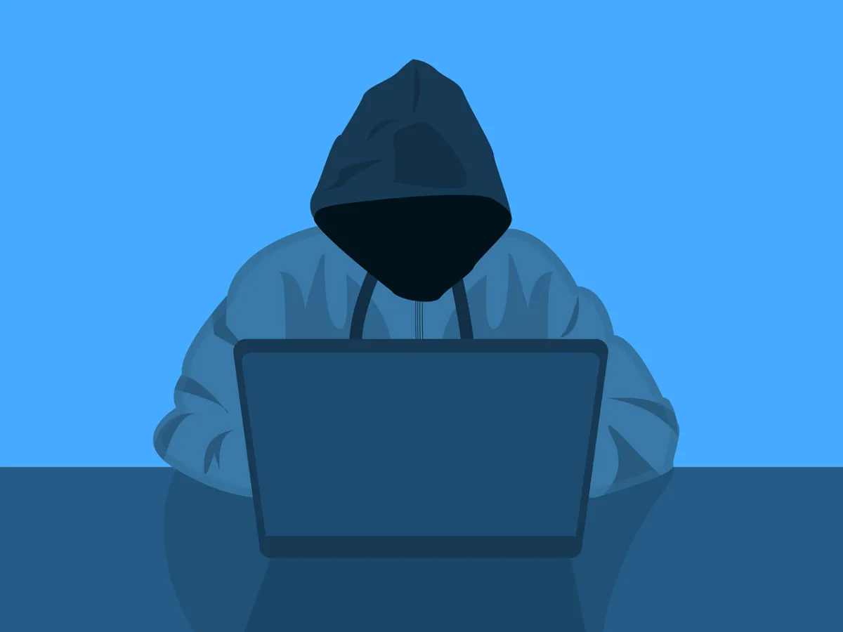 A person in a hoodie sitting at a table hacking a computer.