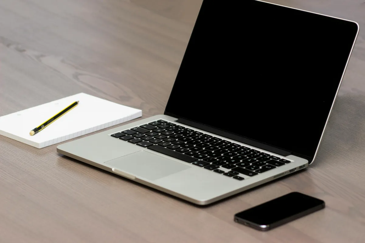 A silver laptop sitting beside a smartphone and a note pad.