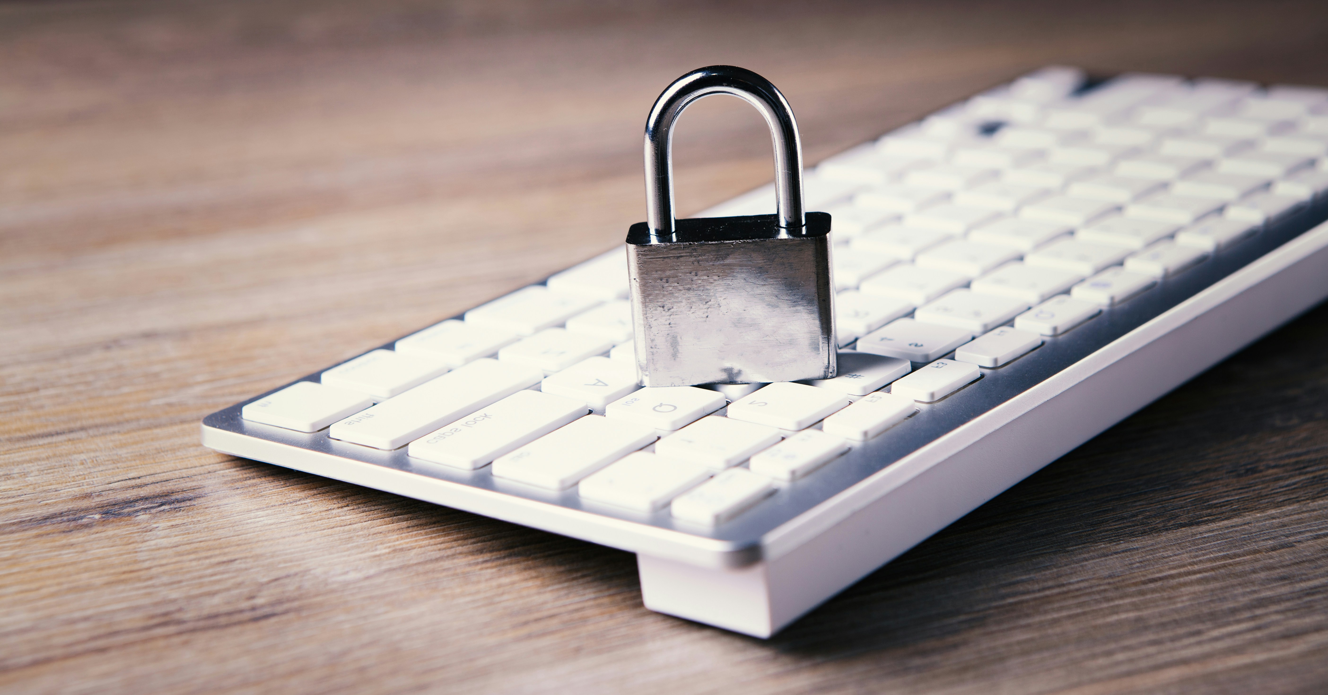 A metal padlock sitting a white computer keyboard.