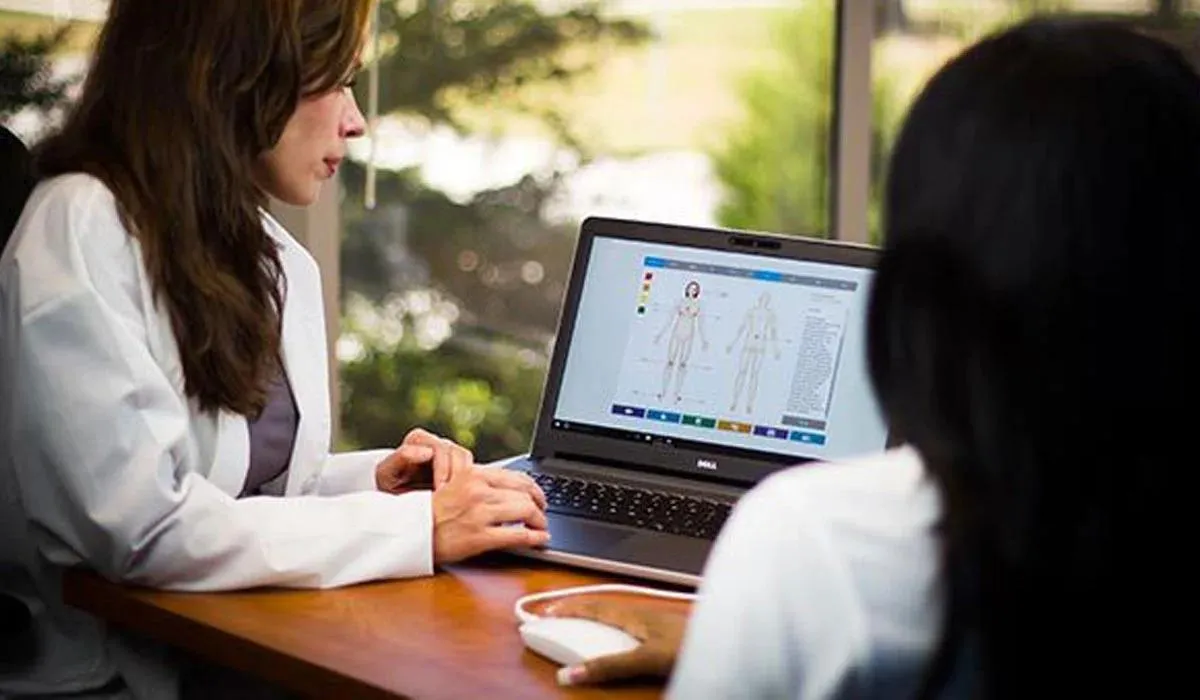A women looking at a computer screen with the results of another women's bioenergetic testing on a desk with another women moving the mouse to navigate the screen