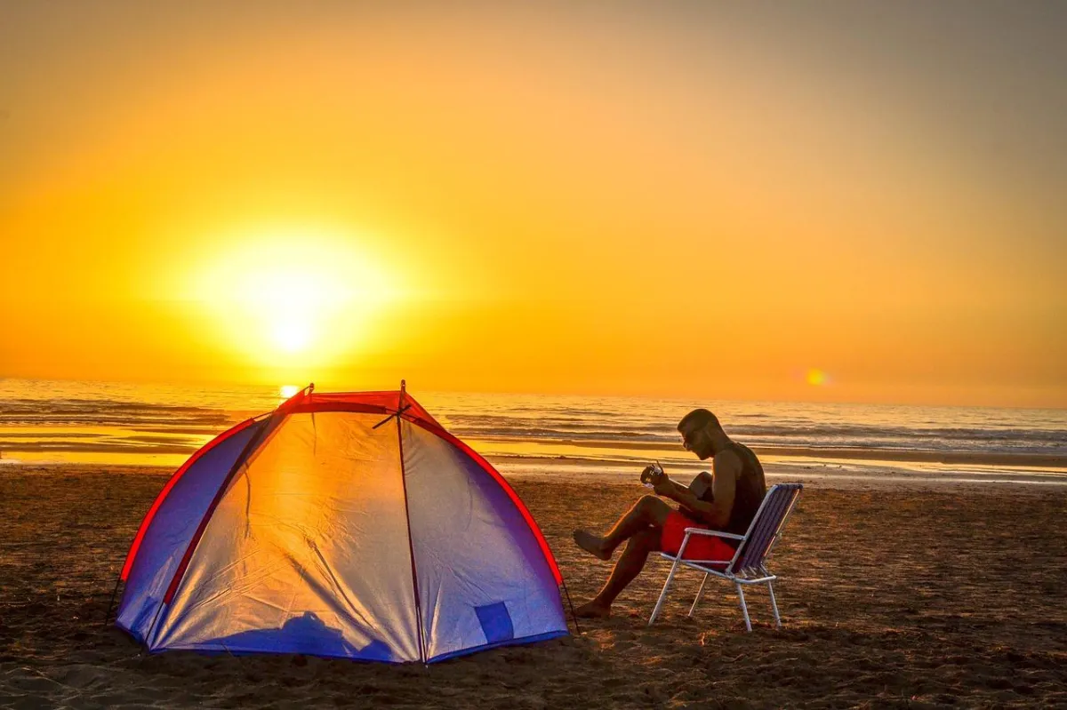 Man camping by the beach, relaxing and playing his guitar, depicting an image of calm and happiness
