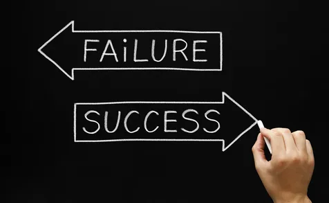 Hand drawing two arrows on a chalkboard — one labeled ‘Failure’ pointing left and one labeled ‘Success’ pointing right, representing mindset and direction in building a successful coaching business.