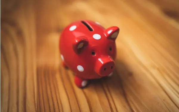 Red polka-dotted piggy bank sitting on a wooden table, symbolizing financial decision-making and personalized pricing strategies for coaches.