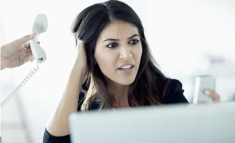 Woman appearing frustrated while multitasking at her desk, symbolizing business stress and burnout.