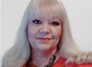 Portrait of a confident woman with long blonde hair wearing a red top and necklace, symbolizing warmth, determination, and professionalism as a relationship coach.