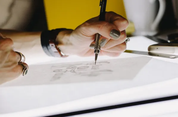 Close-up of a person’s hand sketching creative designs on paper with a pencil.