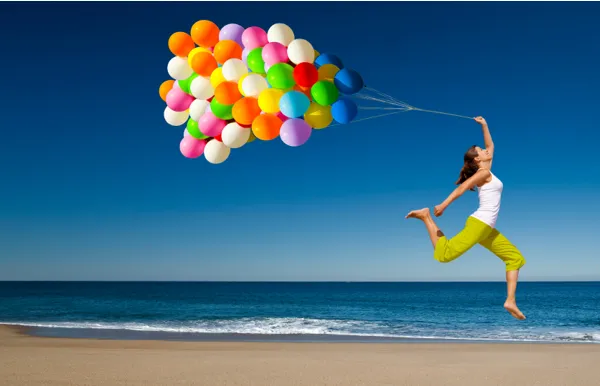 Woman on the beach holding a bunch of colorful balloons, expressing energy and perspective in achieving goals.