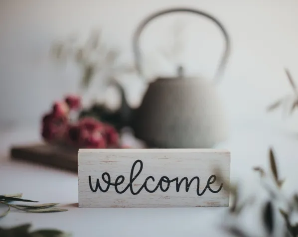 Handcrafted welcome sign in cozy setting with flowers and teapot, representing community and invitation