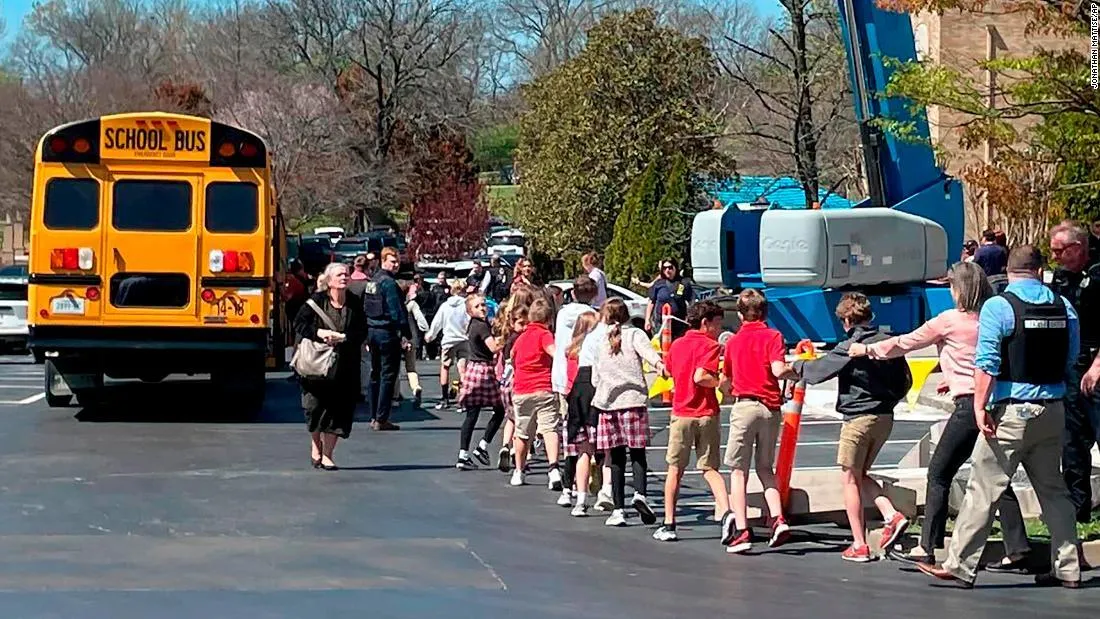 Children holding hands in a chain walking away from school grounds after the Nashville Presbyterian Chrch school shooting accompanied by law enforcement officers