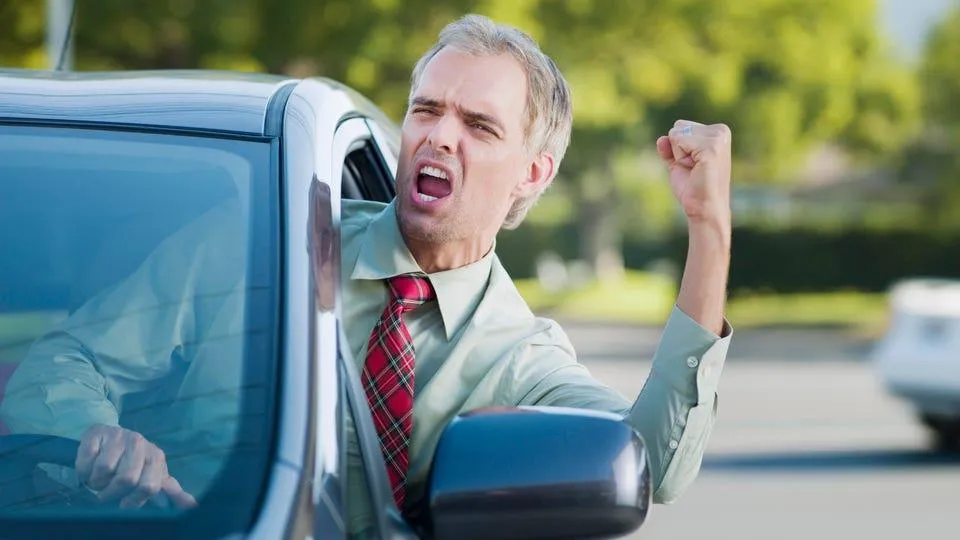 a man sticking his body out of his car window and waving his arm in anger