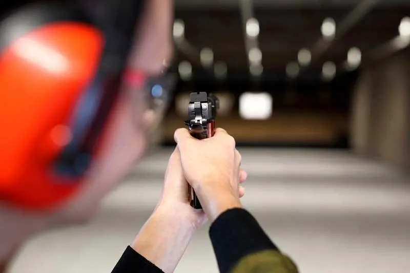 Lady at shooting range aiming a pistol at a paper target