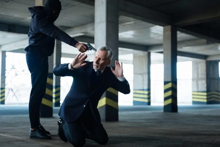 a masked man holding a man in a suit at gun point in a parking garage