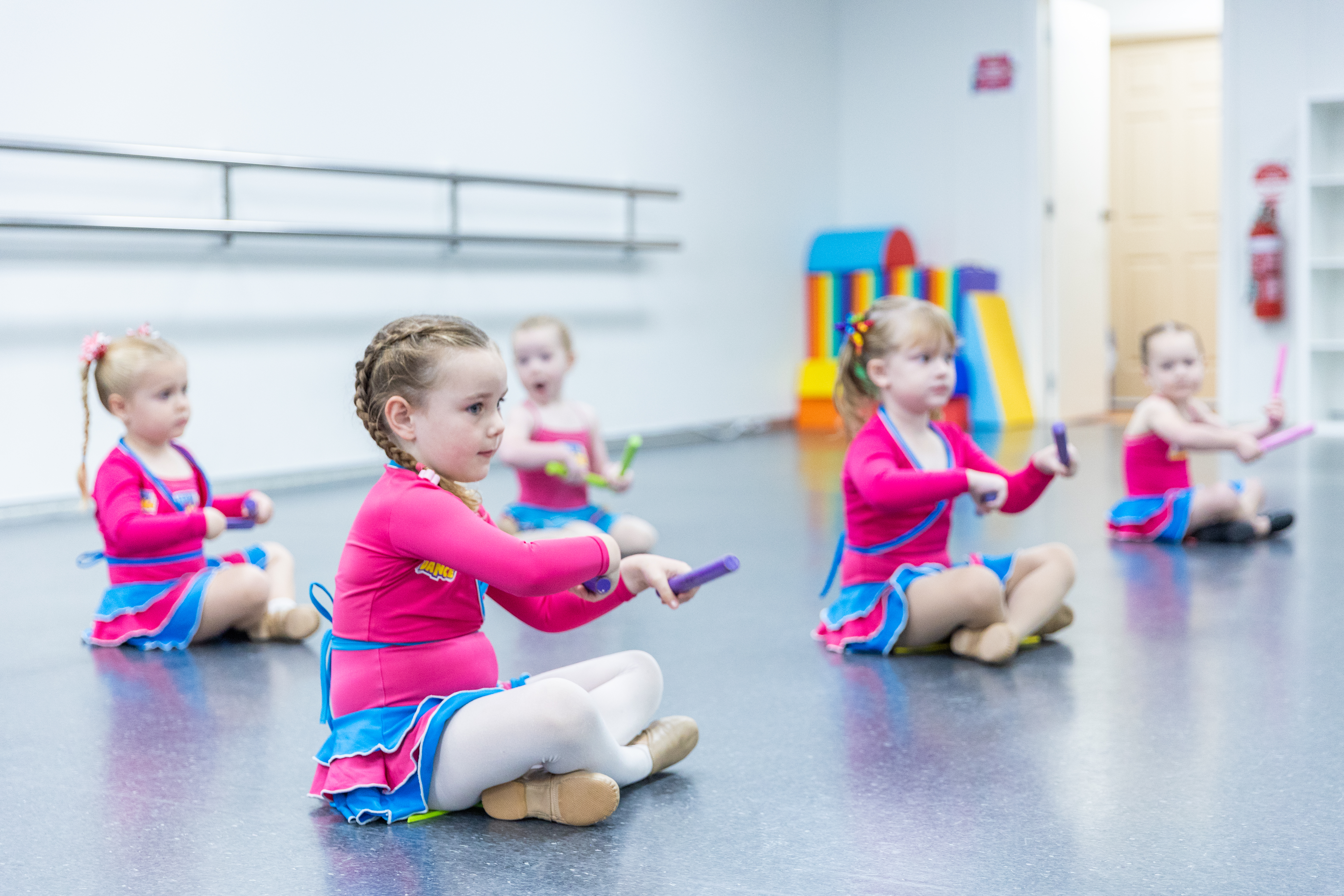 Preschool dancers sitting on the floor practising simple movements with props, developing coordination, focus, and early dance foundations.