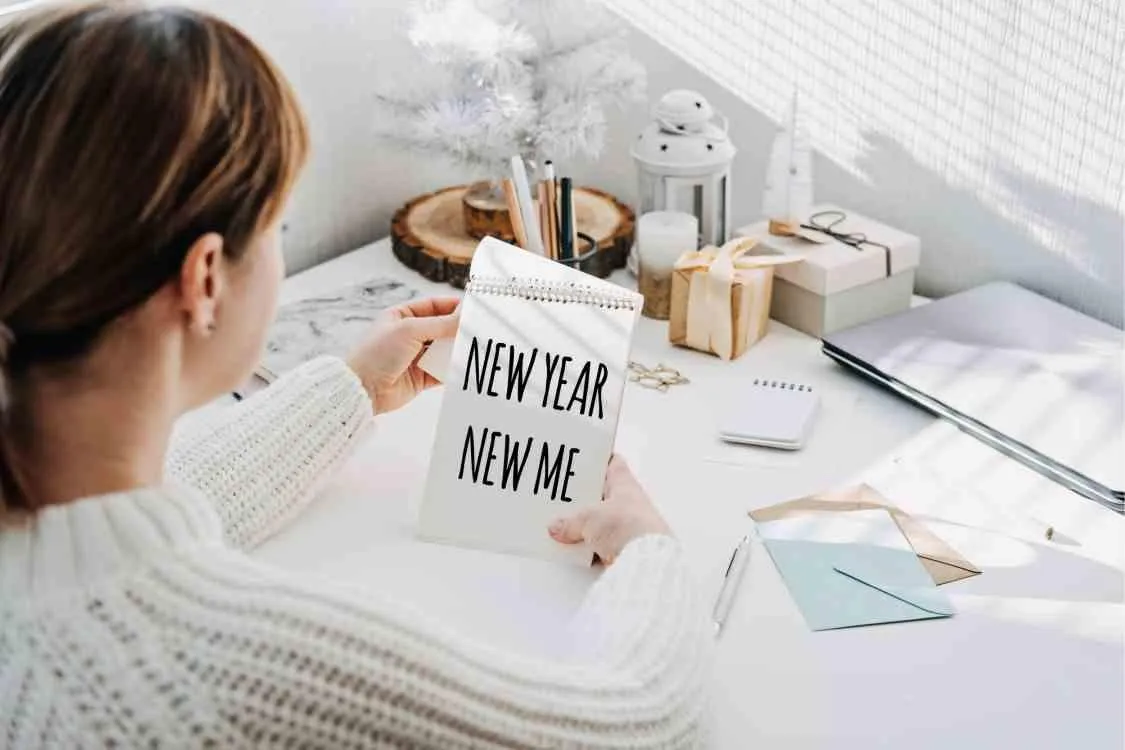 NEW YEAR NEW ME text in open notepad in womans hand on table at home. Setting goals and new years resolution. New year loading.