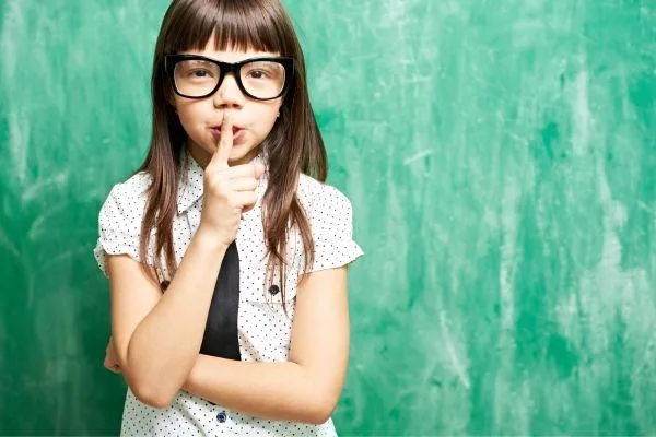 young girl impersonating teacher with hands to lips to be quiet