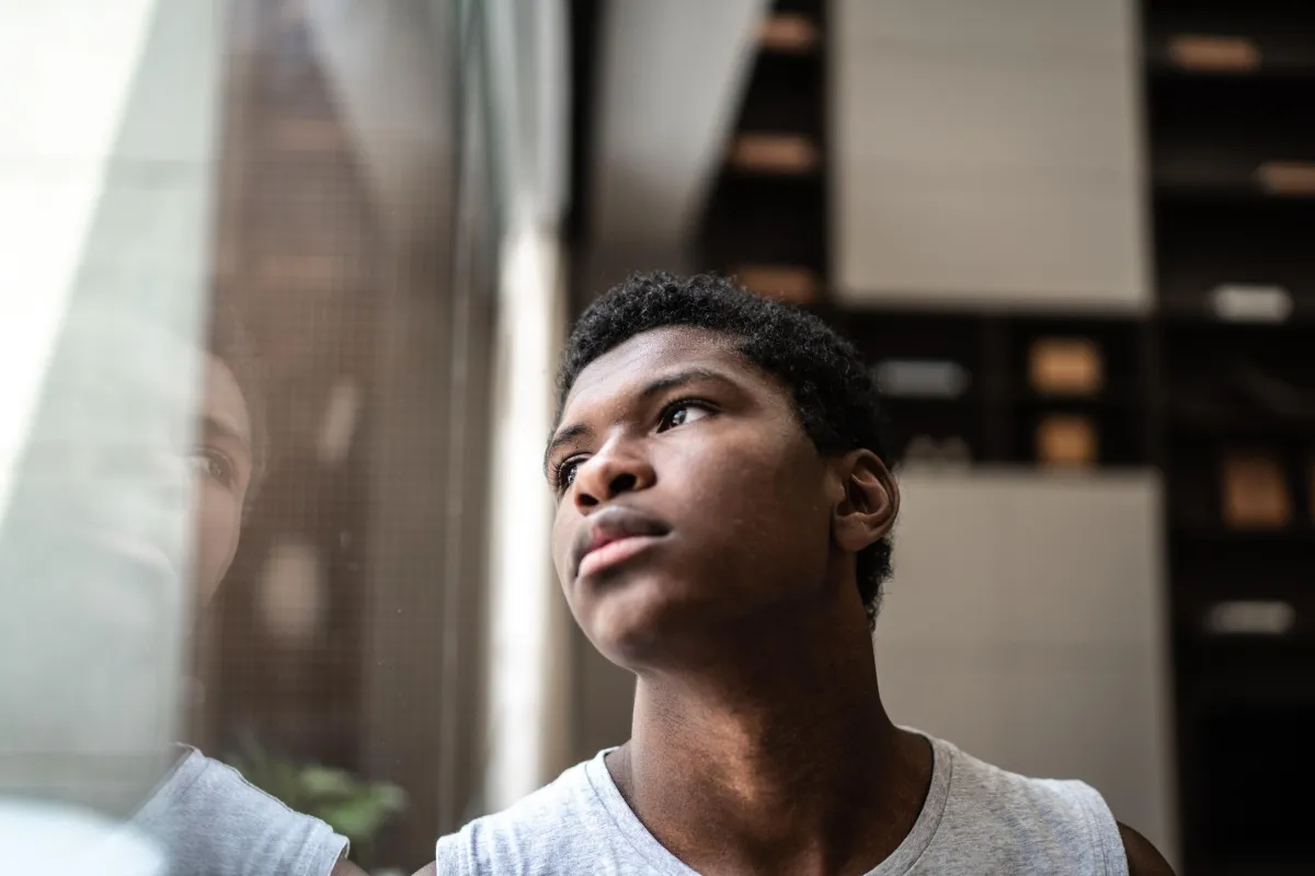 Young black man looking out window with a worried face