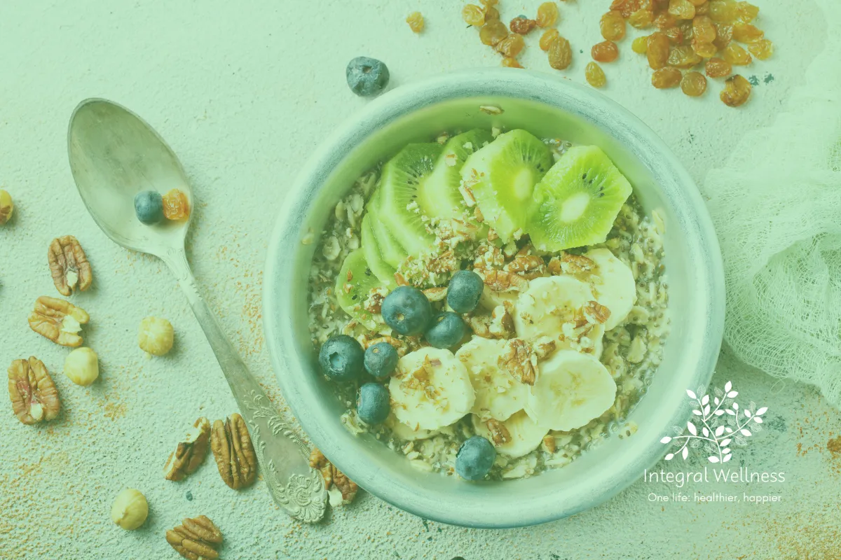Healthy bowl of oatmeal topped with kiwi, banana, blueberries, nuts, and seeds, with the Integral Wellness logo in the corner.