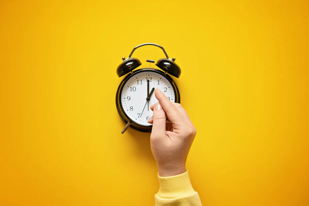 A hand changing the time on an old style alarm clock