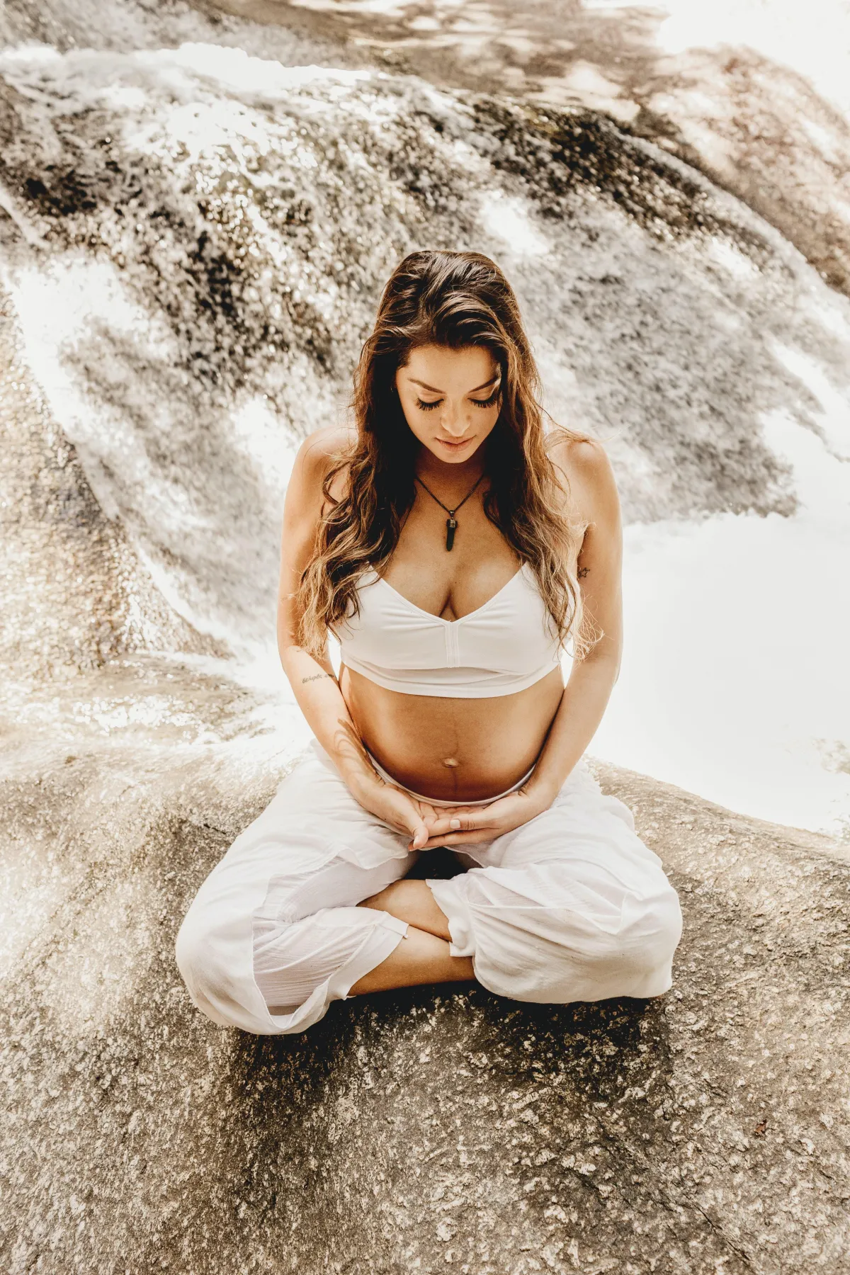 Expectant mother practicing mindfulness in a serene outdoor setting, surrounded by nature, with a peaceful expression and hands gently resting on her belly