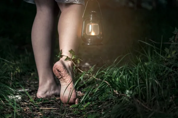 Bare feet caked in mud walking through a dark forest, person holding a glowing lantern