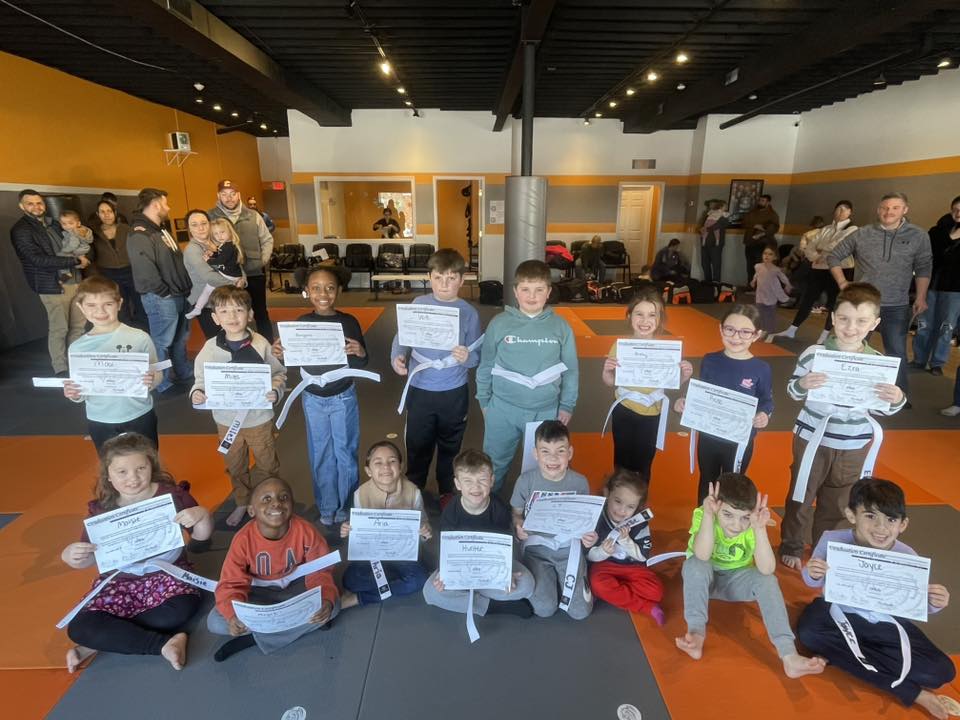 Children holding certificates after a martial arts milestone ceremony at Mastery Martial Arts, celebrating confidence, focus, and personal growth together.