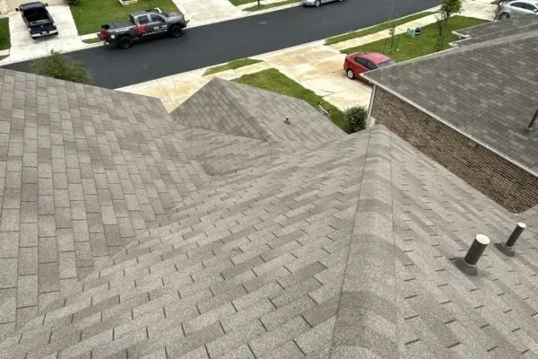 Clean, recently installed asphalt shingle roof on a residential home, viewed from the ridge line, with roof vents and neighborhood streets visible below.