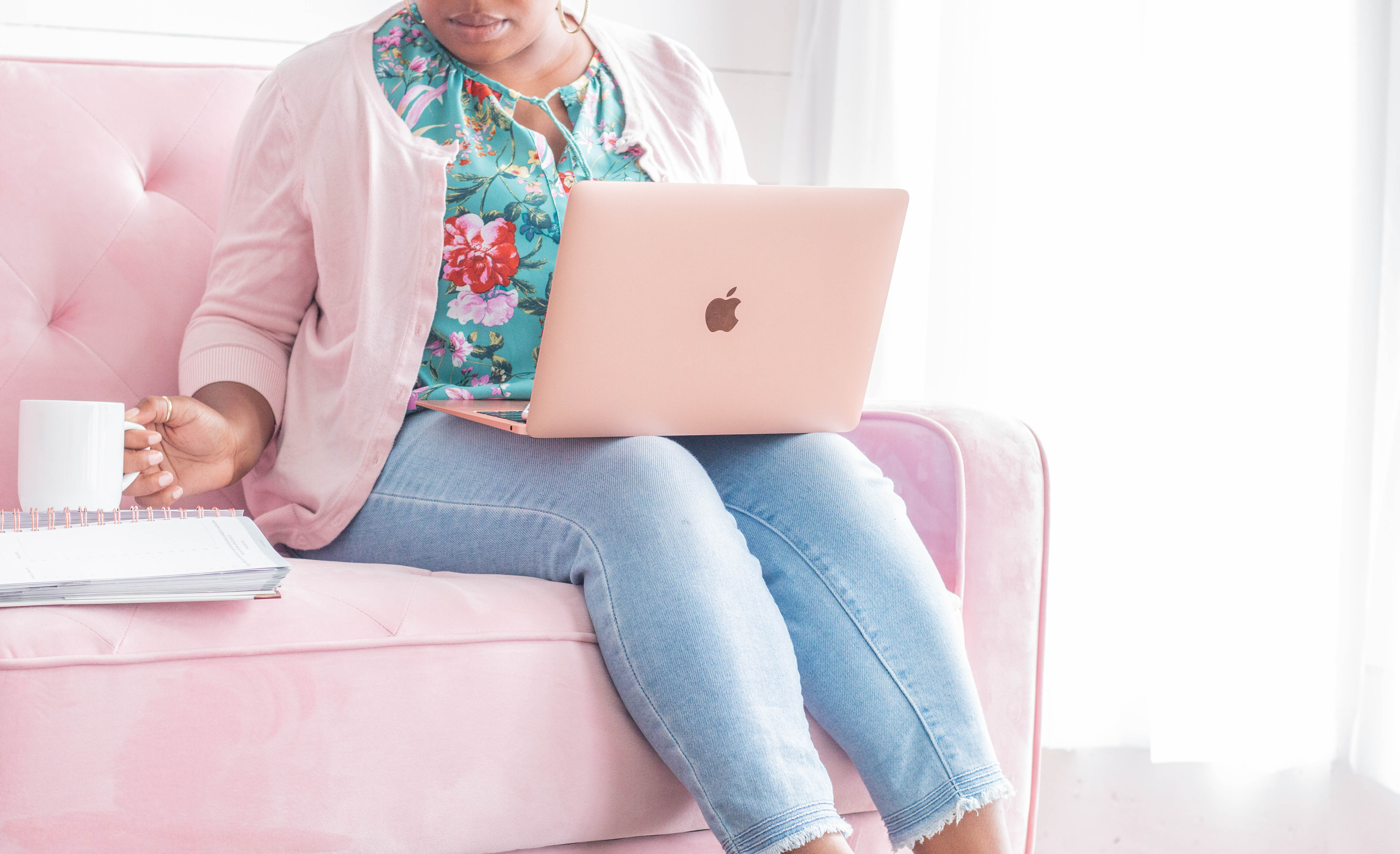 woman sitting on pink coach with laptop on lap