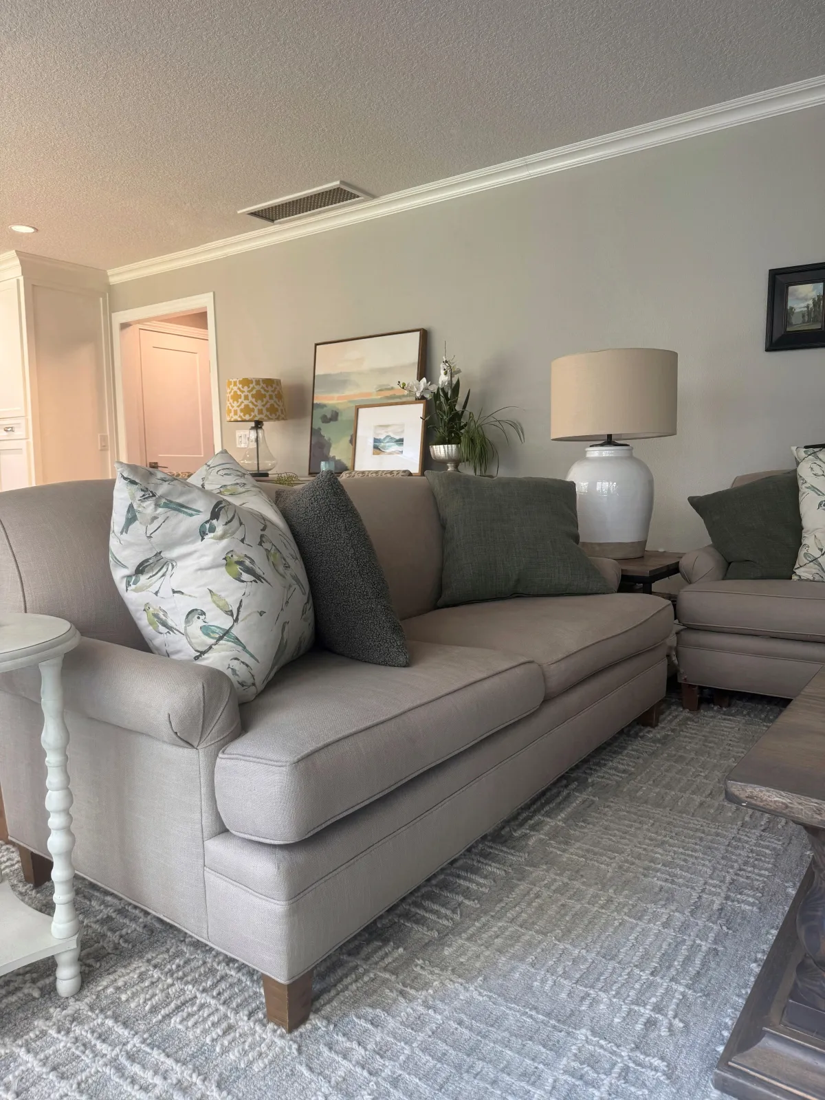A neutral-toned living room featuring a sofa with decorative pillows, a textured rug, and accent furniture.