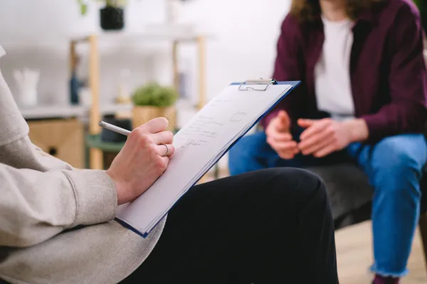 Close-up of a therapist taking notes during a cognitive behavioral therapy (CBT) session with a seated patient, symbolizing professional mental health support in a calm clinical setting.