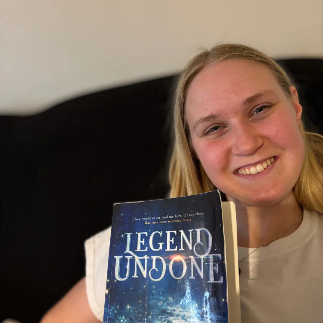 Happy reader holding Legend Undone clean romantasy paperback book