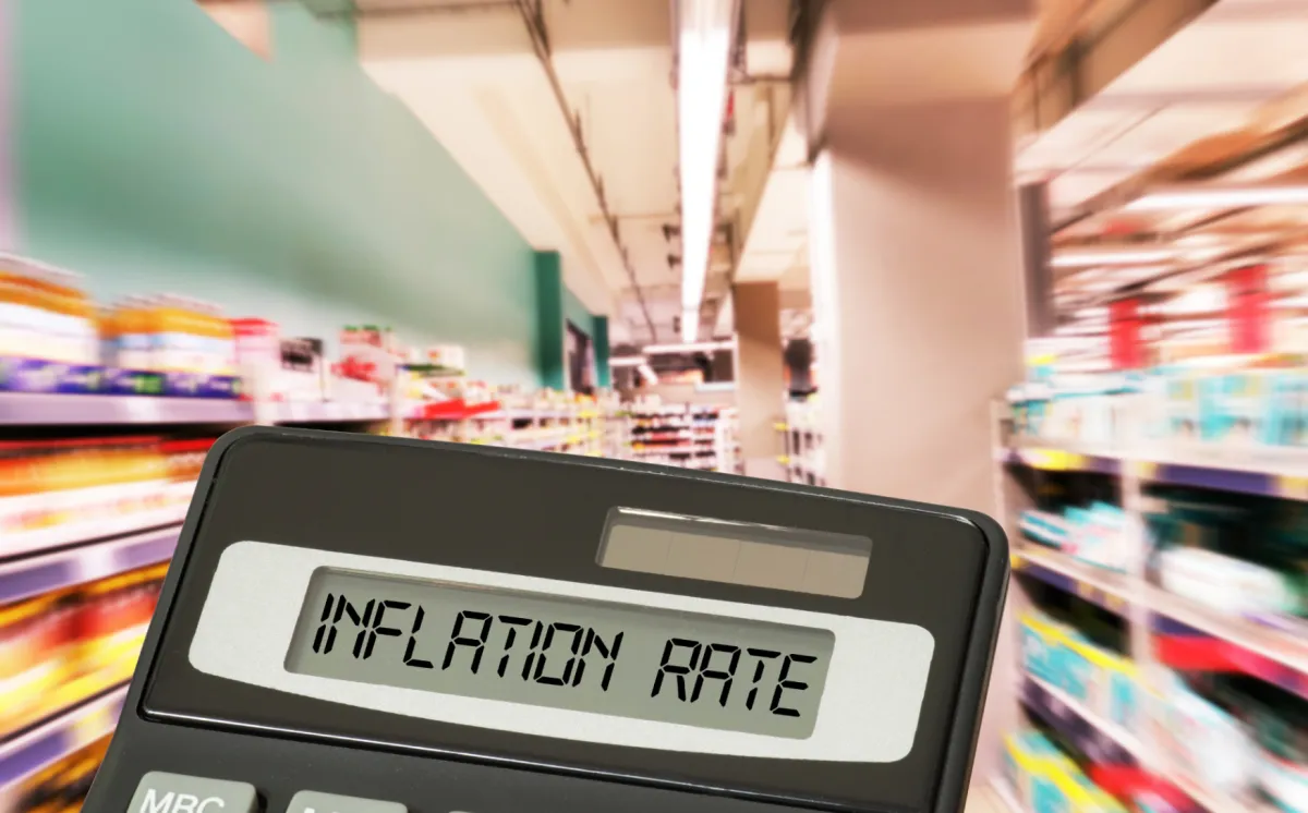 Calculator showing inflation rate in a supermarket aisle, symbolizing rising grocery prices and budgeting challenges in 2025.