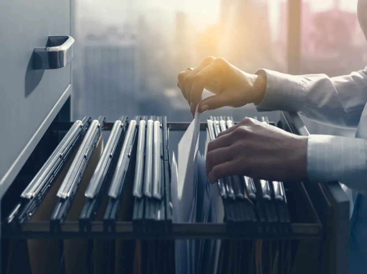 A woman in business attire withdraws paperwork from a filing cabinet