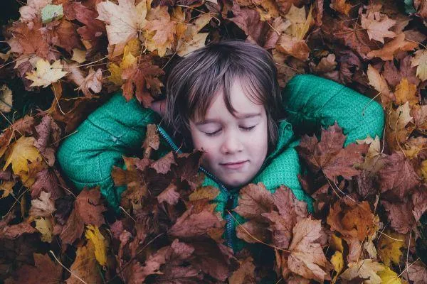 Child lying peacefully in autumn leaves, exploring nature and place-connected learning in early childhood sustainability education.