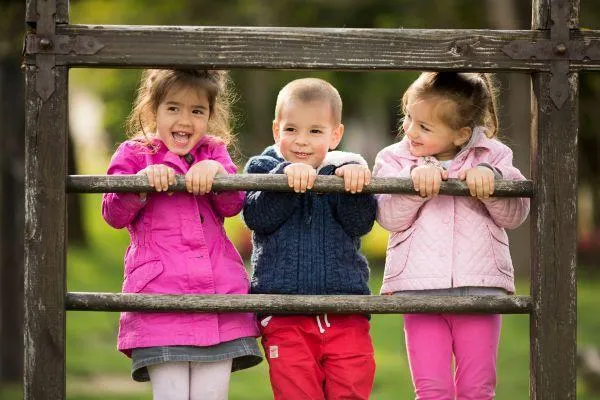 Three young children smiling and playing outdoors, showing why place and nature matter for sustainability learning in early childhood education.