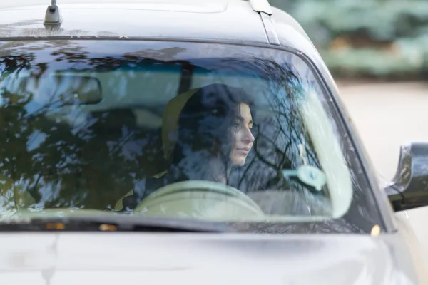 A photo of a woman sitting in her parked car looking at the dashboard — contemplative, not defeated.