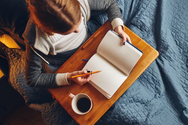 A woman sitting with a journal and a cup of coffee