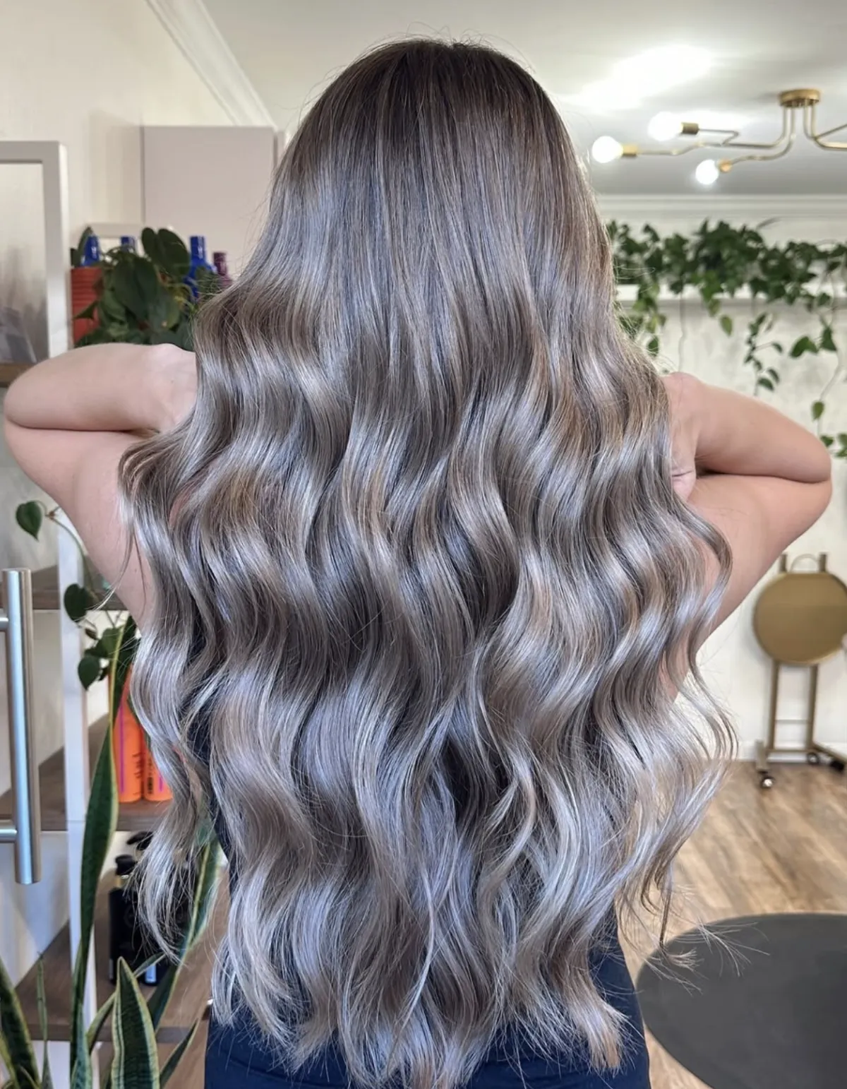 Long smoky ash blonde balayage styled in defined waves, showing cool blended tones and dimensional finish in a salon setting.