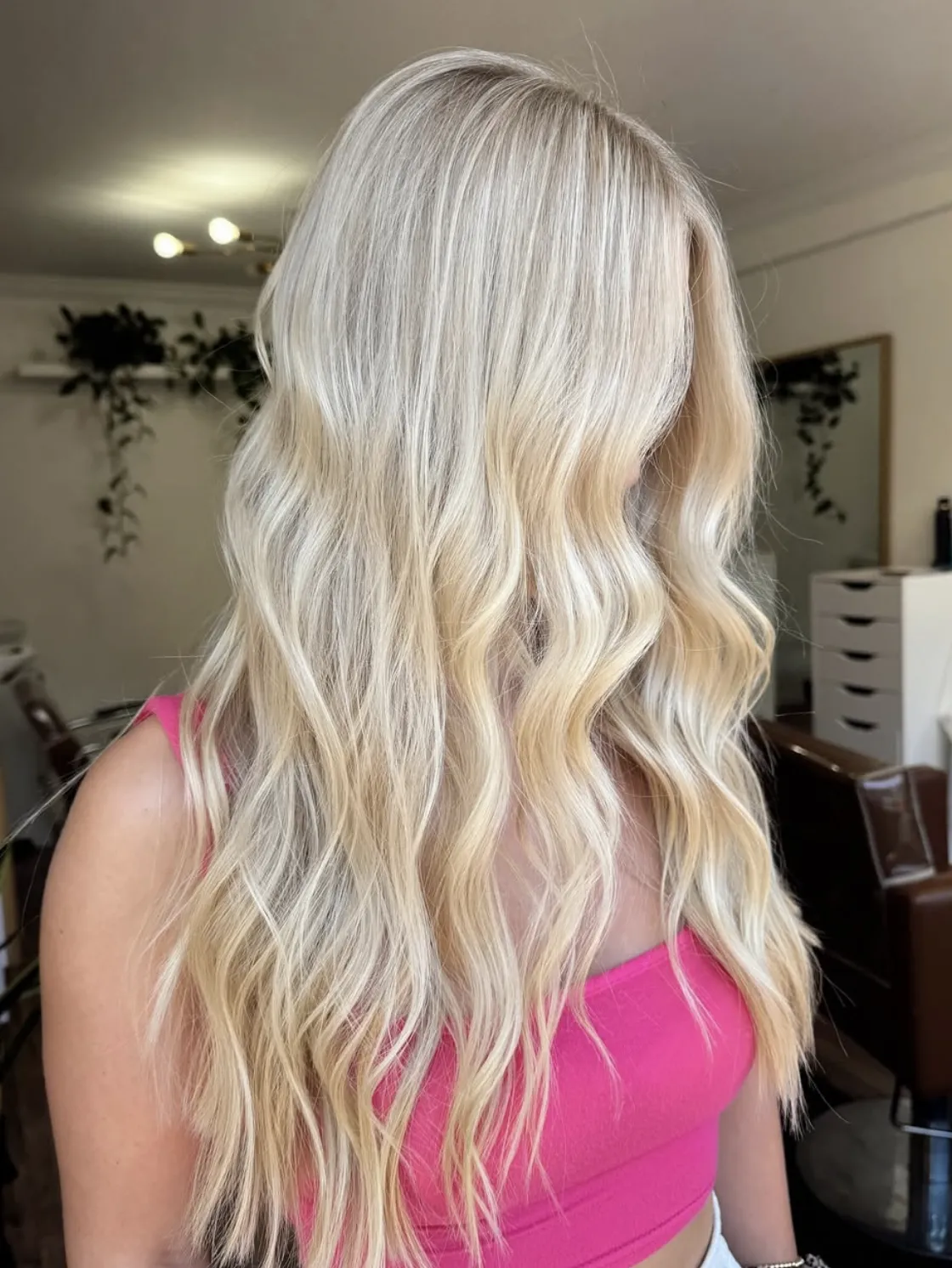 Long bright blonde balayage styled in soft beach waves, showing smooth blend and dimensional tone in a salon environment.