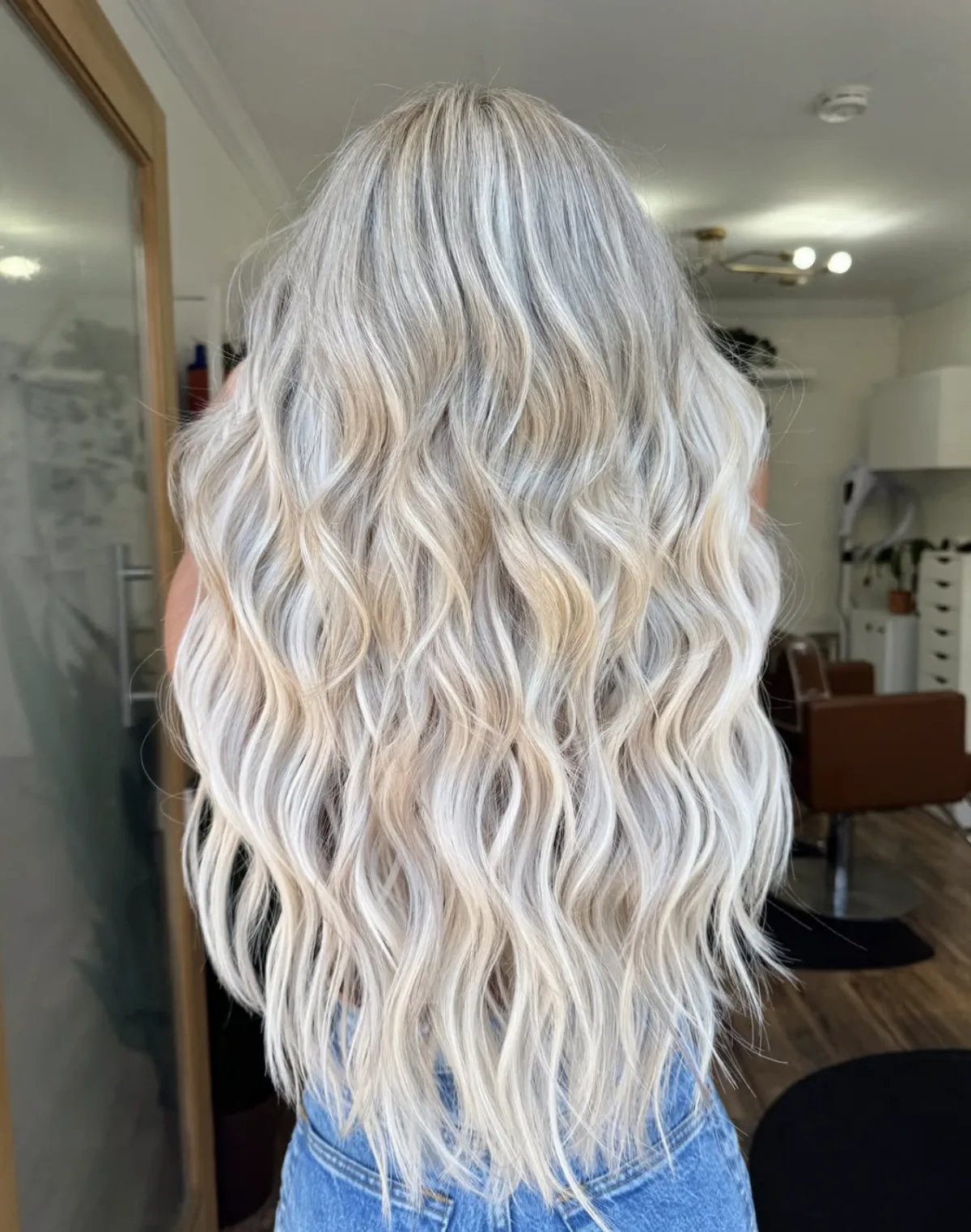Long platinum blonde balayage with soft waves, showing blended highlights and dimensional tone styled in a salon interior.