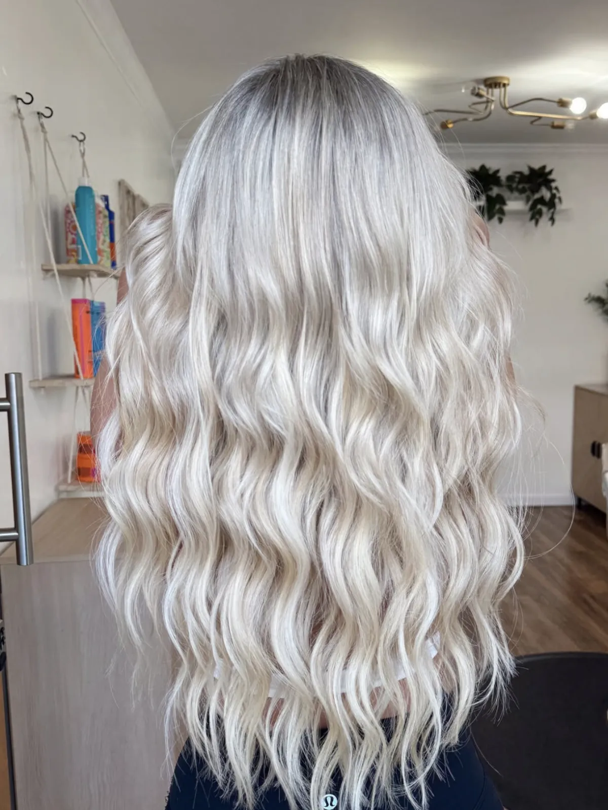 Long platinum blonde balayage styled in loose waves, showing smooth blend and dimensional finish in a salon setting.