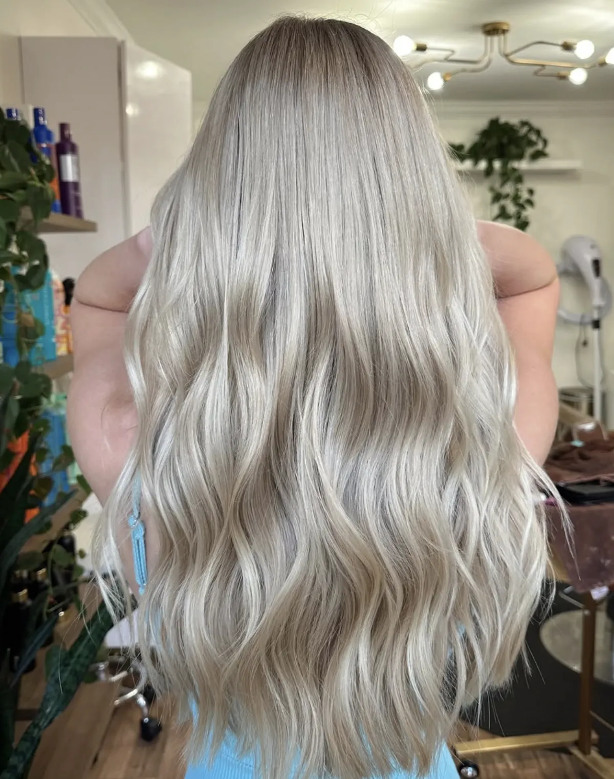 Long icy blonde balayage styled in soft waves, showing smooth blend and dimensional tone in a professional salon setting.
